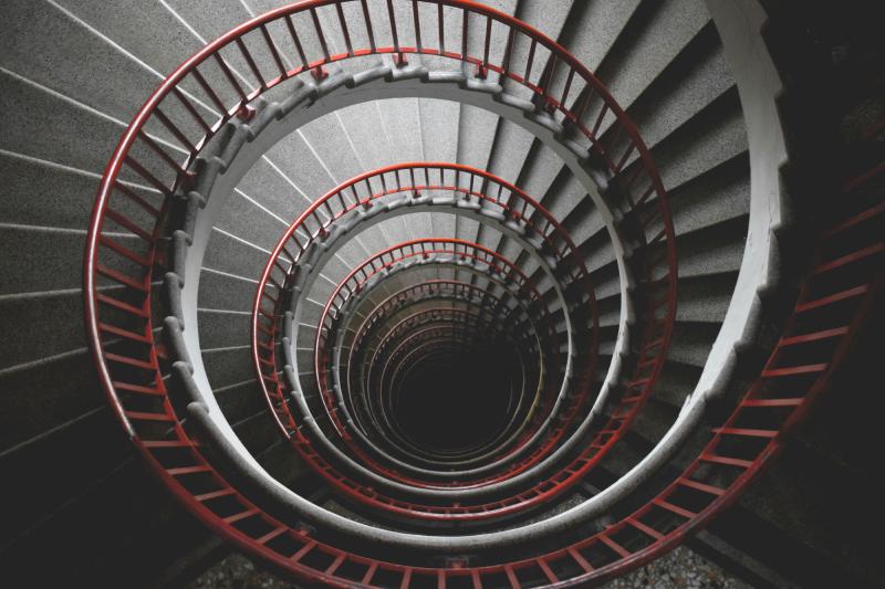 A dark spiral staircase seen from above, descending into shadow
